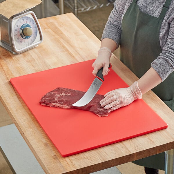 A woman wearing gloves cutting meat on a red Thunder Group cutting board.