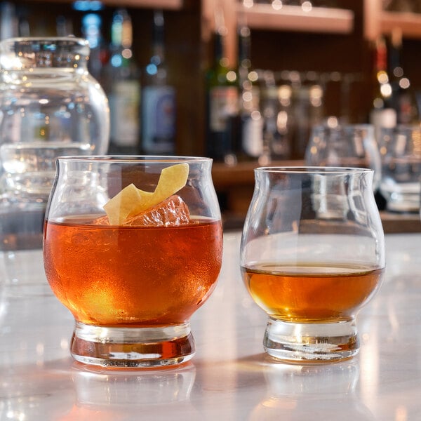 Two Reserve by Libbey bourbon tasting glasses filled with brown liquid and ice on a table.