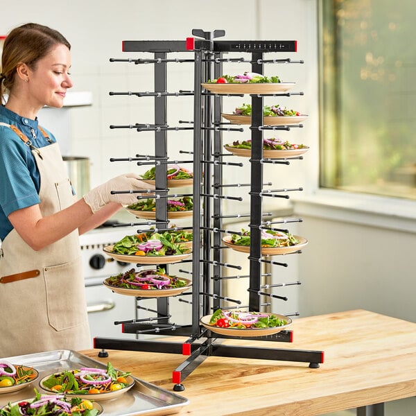 A woman in an apron and gloves putting plates of salad on a JackStack countertop rack.