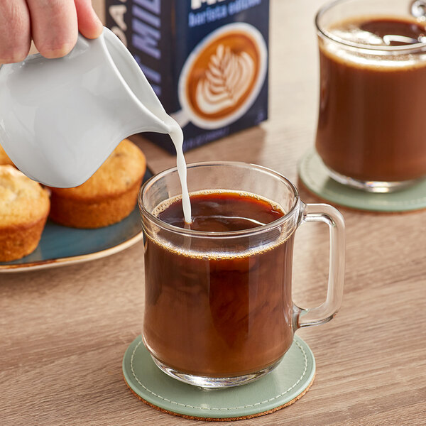 A person pouring Mooala Barista Oat Milk into a glass of coffee.