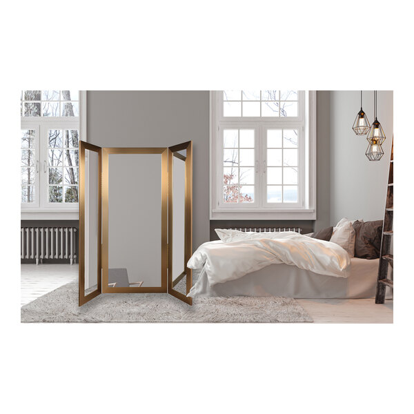 A room with a BrandtWorks gold trifold dressing mirror on the floor.