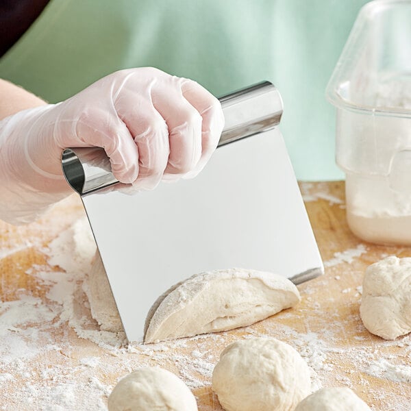 A person using a Choice stainless steel dough cutter to cut dough on a table.
