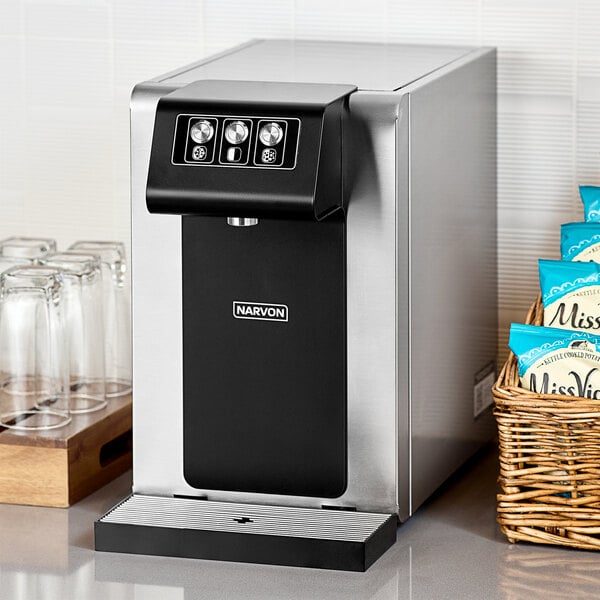 A black and silver Narvon countertop water dispenser next to a glass.