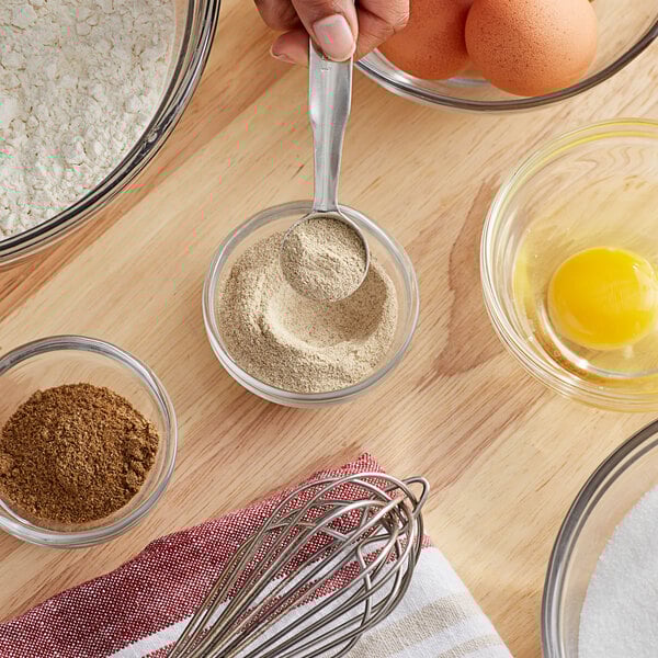 A person holding a spoon with a spoonful of white powder over a bowl of eggs and flour.