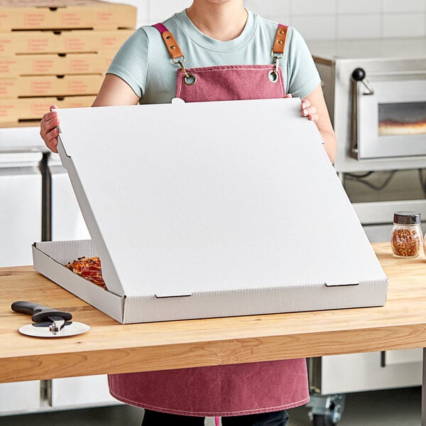 A woman holding a white Choice pizza box in front of a pizza oven.