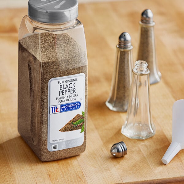 A bottle of McCormick Culinary Pure Ground Black Pepper on a counter next to salt and pepper shakers.