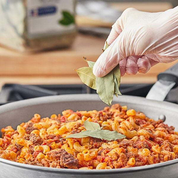 A person holding a McCormick Culinary Bay Leaf over pasta in a skillet.