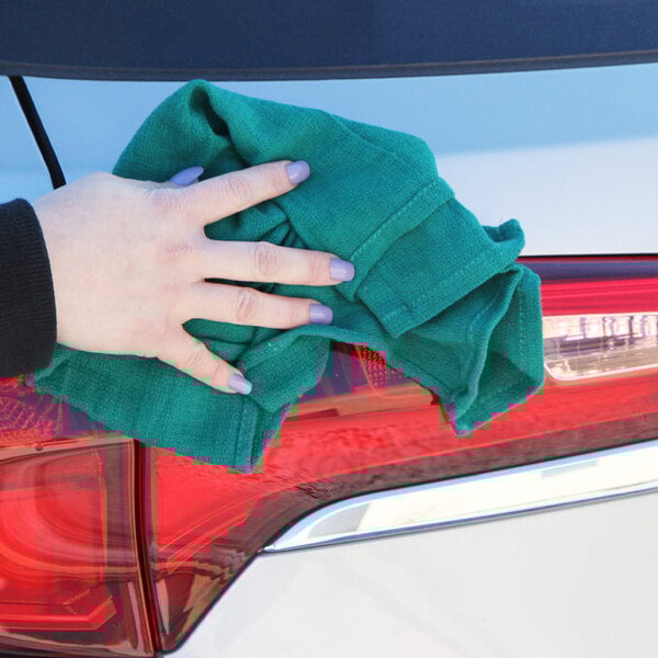 A hand holding a Monarch Brands hunter green cotton huck towel.