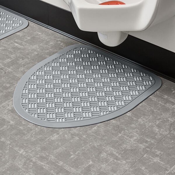 A bathroom with a urinal and a sink with a Lavex Gray Disposable Urinal Floor Mat on the floor.