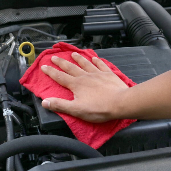 A hand with a Monarch Brands red shop towel cleaning a car engine.