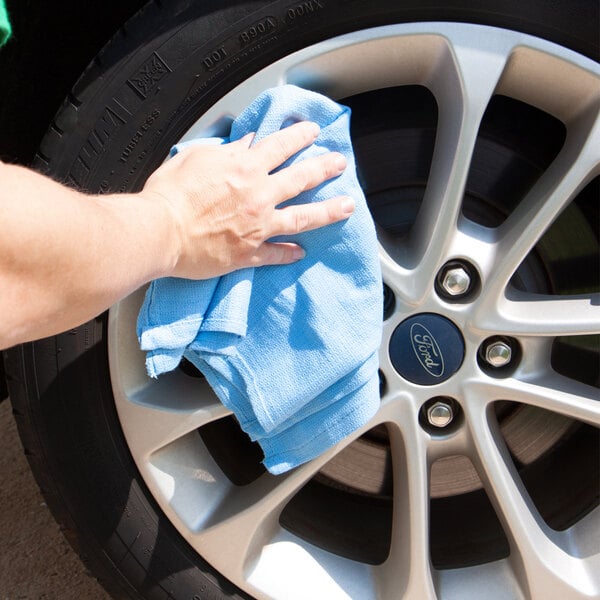 A person cleaning a wheel with a blue Monarch Brands huck towel.
