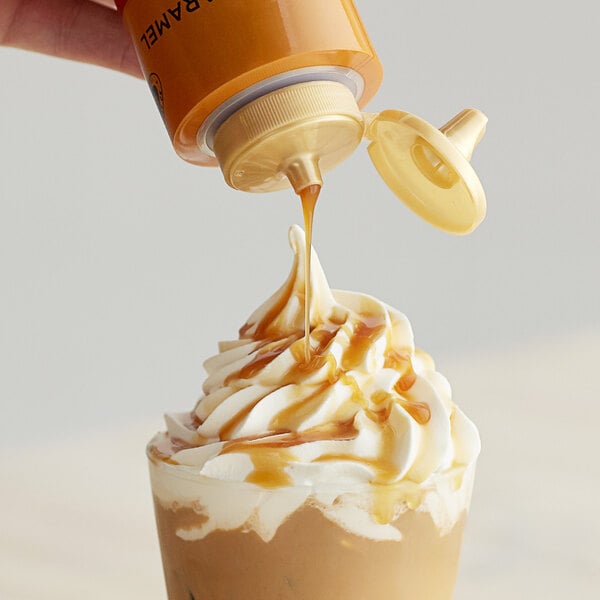 A person pouring Torani Puremade Caramel Flavoring Sauce into a cup of whipped cream.