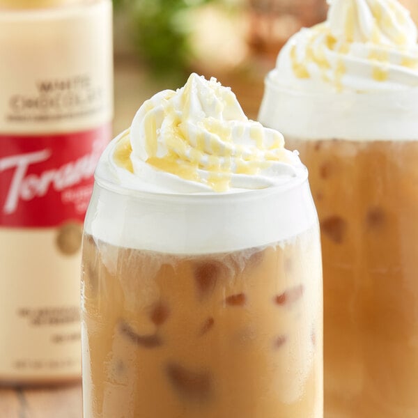 Two iced coffee drinks with whipped cream and Torani white chocolate sauce in a glass.