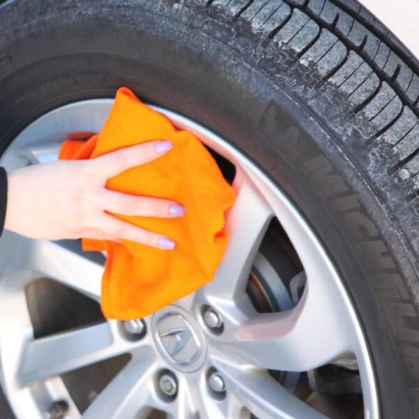 A hand cleaning a wheel with an orange Monarch Brands huck towel.