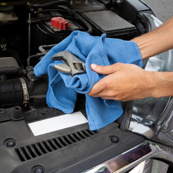A person cleaning a car engine with a blue Monarch Brands recycled cotton wiper.