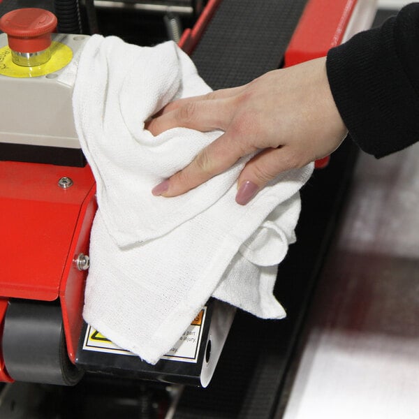 A person's hand holding a Monarch Brands white huck towel.