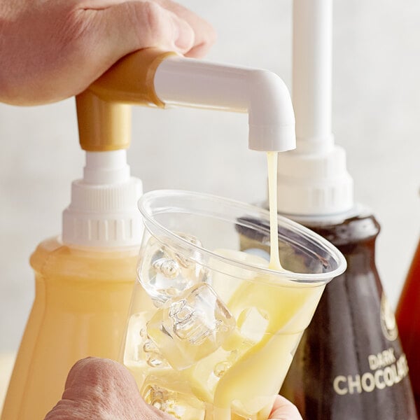 A hand pouring Torani White Chocolate flavoring sauce into a cup.