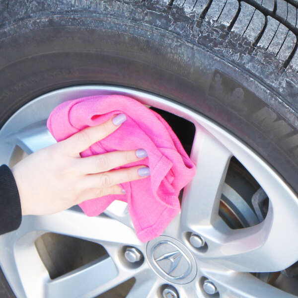 A hand using a pink Monarch Brands huck towel to clean a car tire.