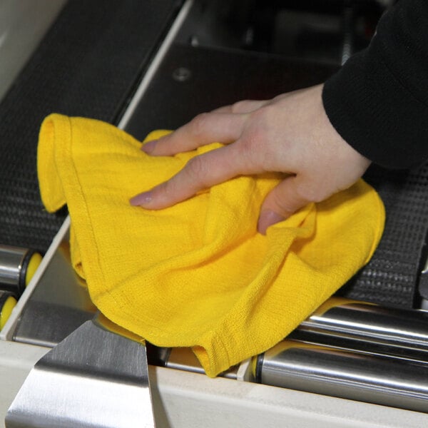 A hand using a yellow Monarch Brands huck towel to clean a machine on a counter.