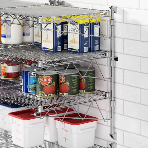 A Regency stainless steel wall-mount shelf with food items on it including cans, white containers, and a bottle.