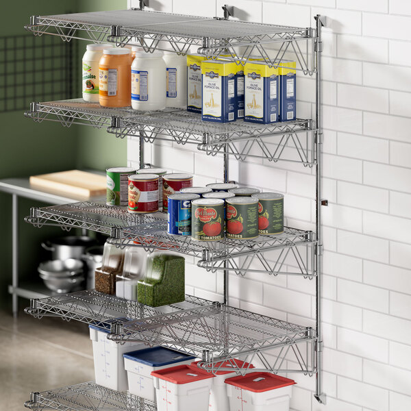 A Regency stainless steel wall-mount shelf post in a professional kitchen with shelves of food.