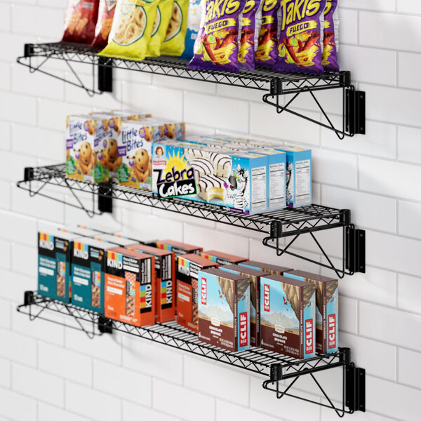 A Regency black epoxy wall-mount wire shelf with snacks and drinks on it.