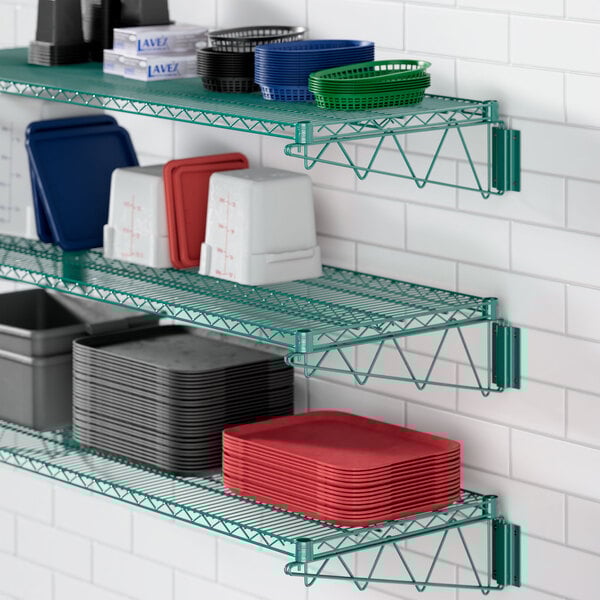 A Regency green metal wire shelf holding dishes, plates, and cups.