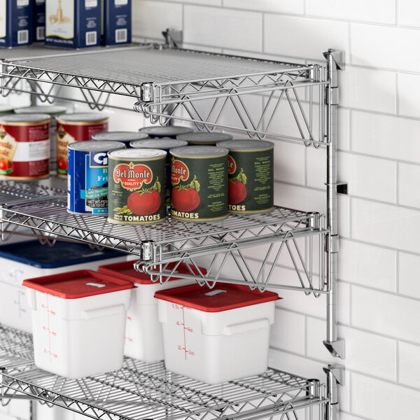 A Regency stainless steel wall-mount shelf with cans and white and red containers on it.