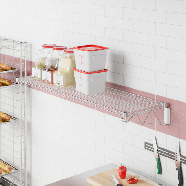 A Regency stainless steel wall-mount wire shelf in a kitchen with clear containers on it.