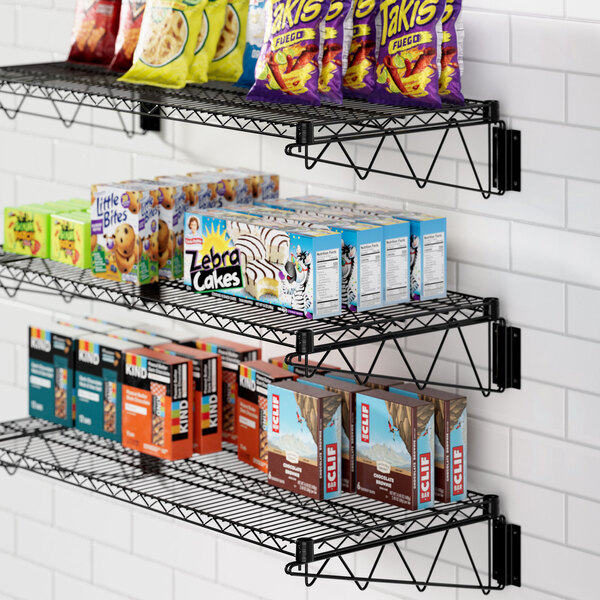 A black Regency wall-mount wire shelf with food and snacks on it.
