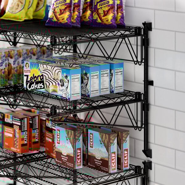 A Regency black wire wall-mounted shelf with snacks and food on it.