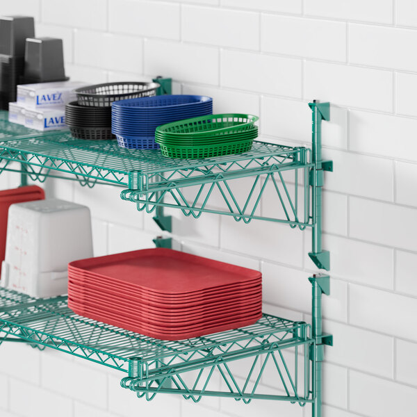 A green metal Regency wall-mounted wire shelf with red and white containers and stacks of red and white plates.