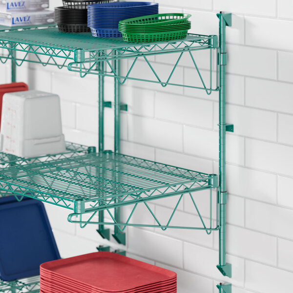 A green metal Regency wire shelf with dishes and utensils on it.