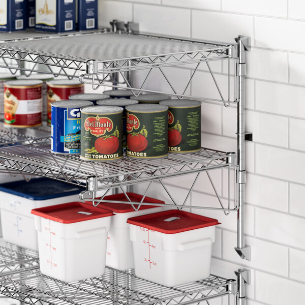 A stainless steel Regency wall-mount wire shelf with food cans and white and red containers on it.