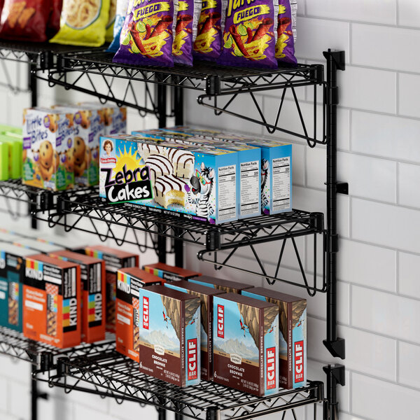 A Regency black wire wall-mount shelf with food and snacks on it.