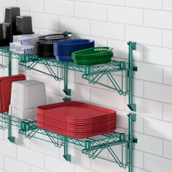 A Regency wall-mounted wire shelf with green epoxy posts holding red plastic plates and bowls.