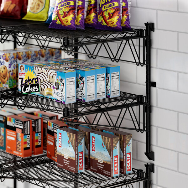 A Regency black wire wall shelf with snacks and drinks on it.