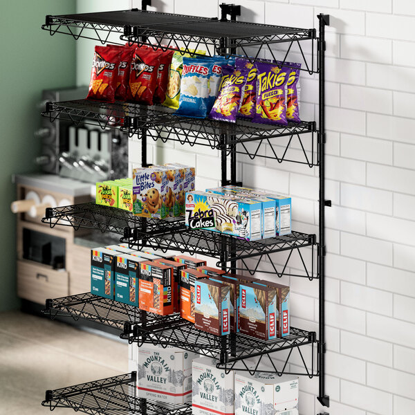 A black metal Regency wall-mount wire shelf with snacks and snacks on it.