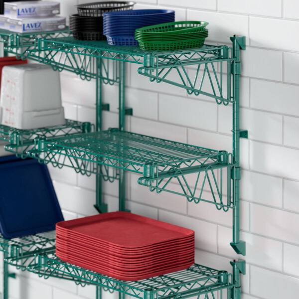 A green metal Regency wall-mounted wire shelf with trays on it.