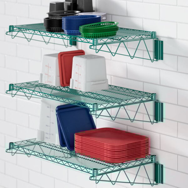 A green Regency wall-mount wire shelf with dishes and plates on it.