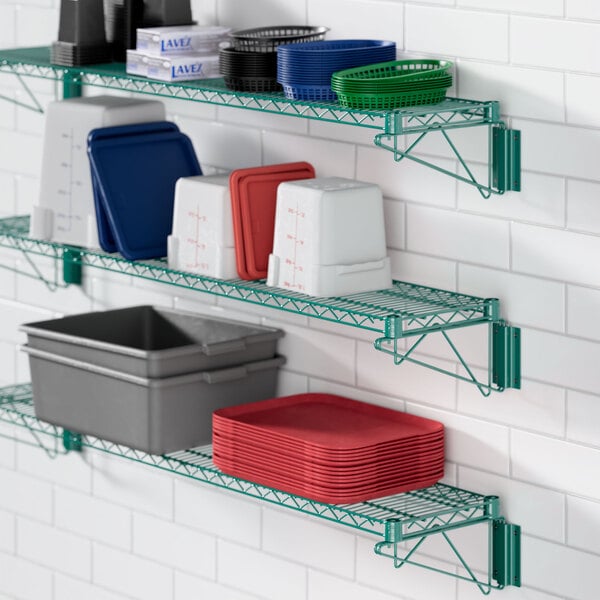 A Regency green wire shelf with dishes, cups and plates on it.