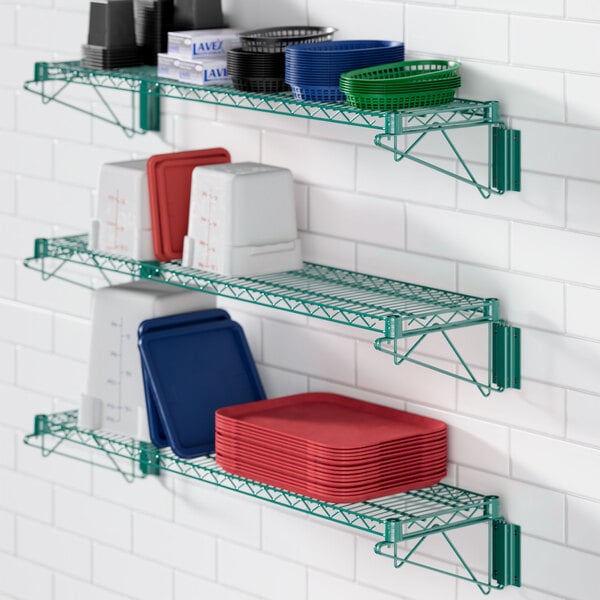 A green Regency wall-mounted wire shelf with dishes and plates on it.