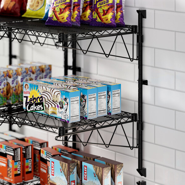 A Regency black wire wall-mount shelf with food and snacks on it.