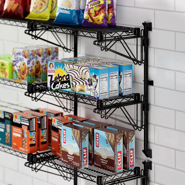 A Regency black wire wall-mount shelf with snacks and drinks on it.