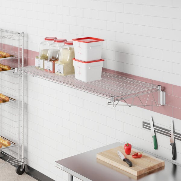 A Regency stainless steel wall-mount wire shelf in a bakery with clear plastic containers with red lids on it.