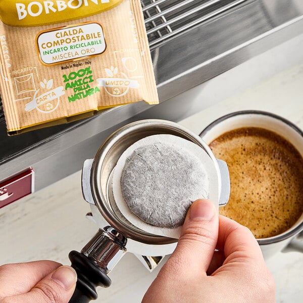 A person's finger placing a Caffe Borbone Gold Blend espresso pod in a coffee machine.