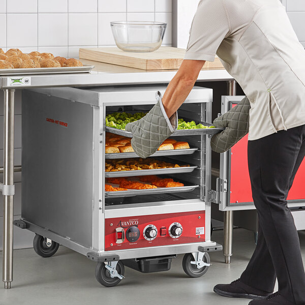 A woman using an Avantco heated holding cabinet to put food inside.