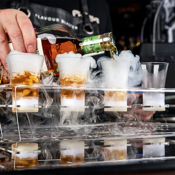 A person using a Flavour Blaster to pour alcohol into plastic shot glasses with smoke coming out.