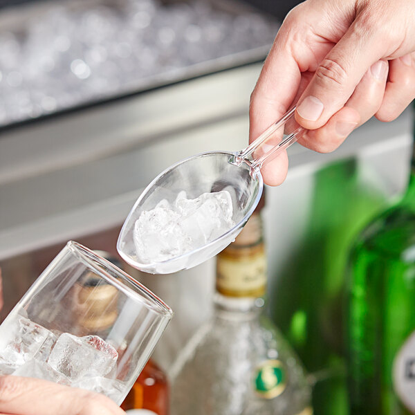 A person using a Visions clear disposable utility scoop to add ice to a glass.