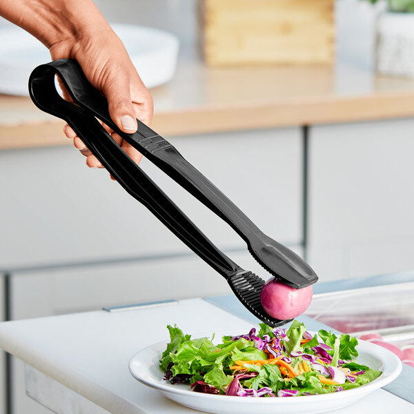 A person using black Choice flat grip tongs to serve salad
